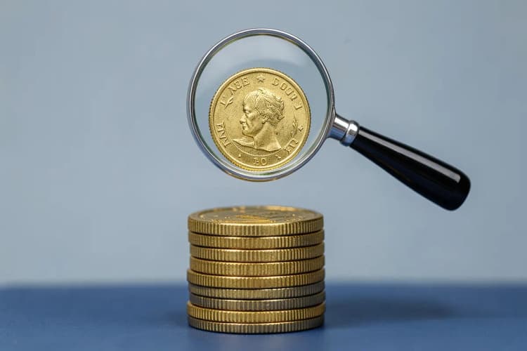 Uma pilha de moedas de ouro com uma lupa examinando uma moeda específica.