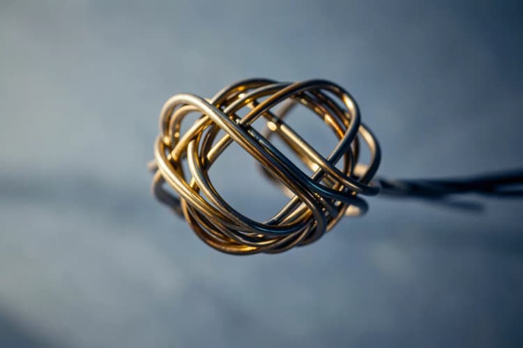 Um nó complexo de fios de metal entrelaçados em close-up, com iluminação dramática vinda de um lado.