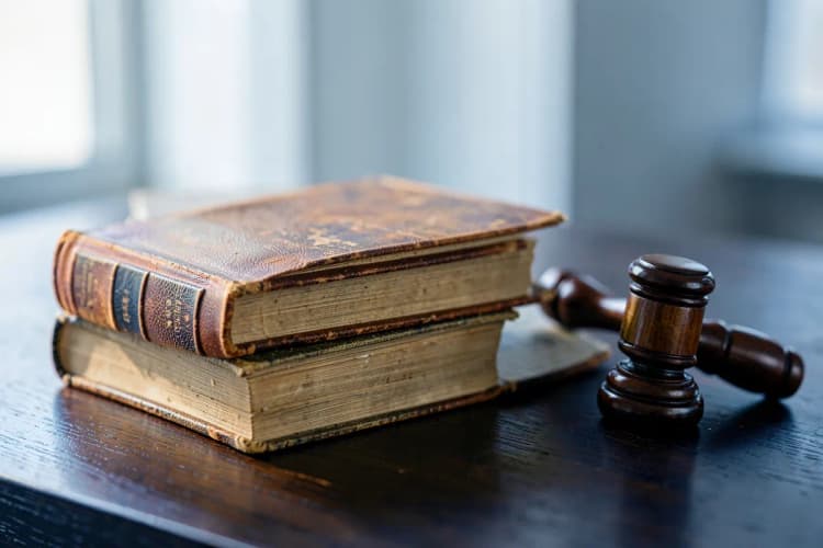 Uma pilha de livros jurídicos antigos e um martelo de juiz sobre uma mesa de madeira escura.