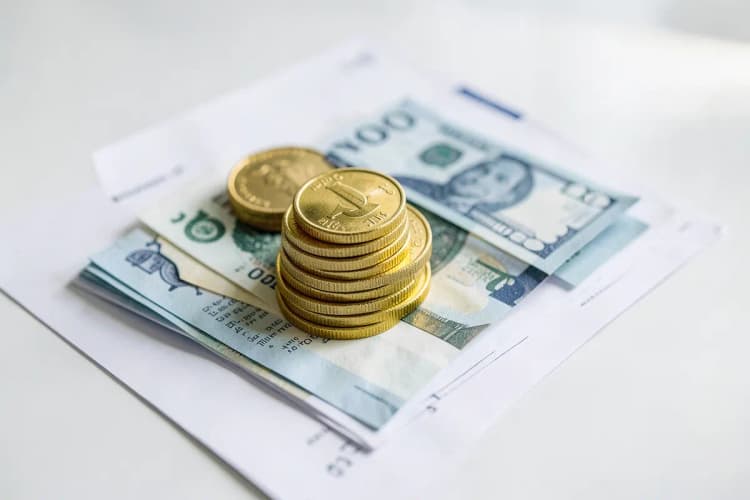 Pilha de moedas de ouro e notas de dinheiro empilhadas em cima de um documento legal, representando dívidas e finanças
