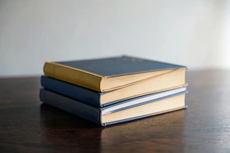 Uma pilha de livros de direito empilhados em cima de uma mesa de madeira escura, com uma balança da justiça sutilmente desfocada ao fundo.
